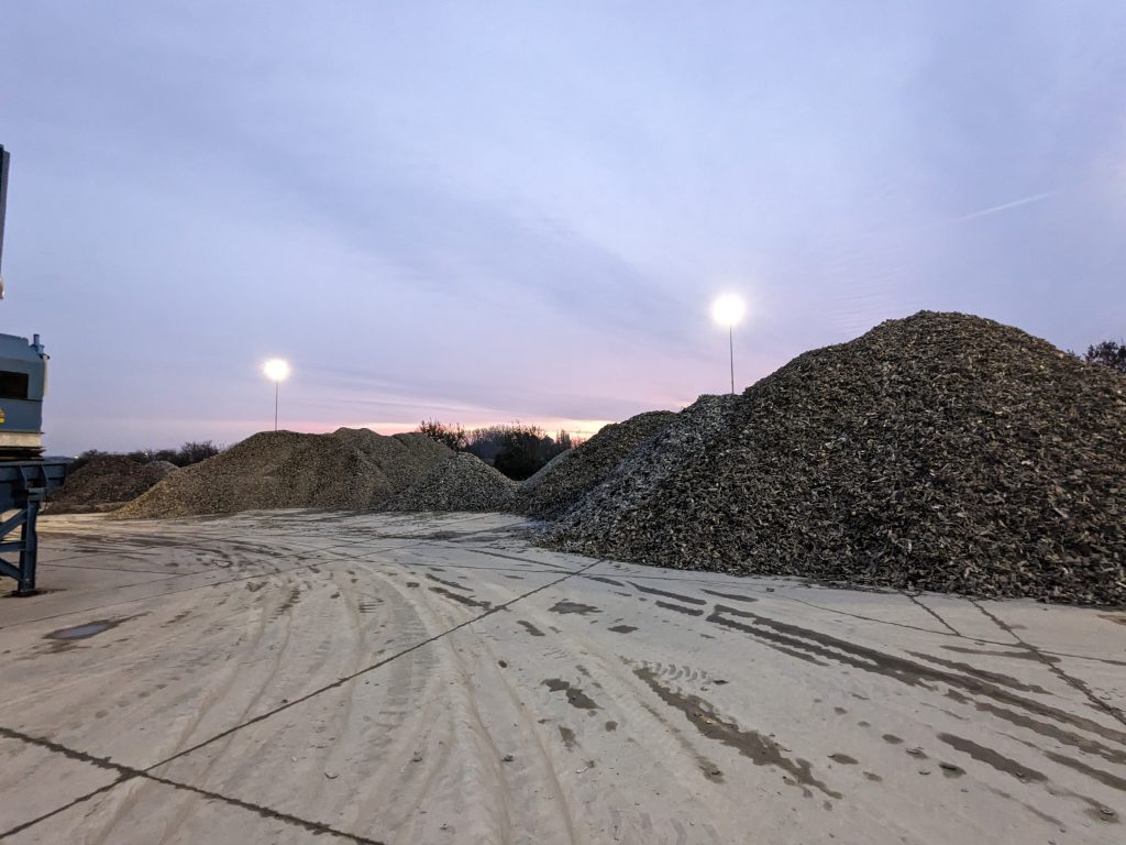 Two piles of shredded metal on a concrete yard at dusk, beside a shredder outfeed